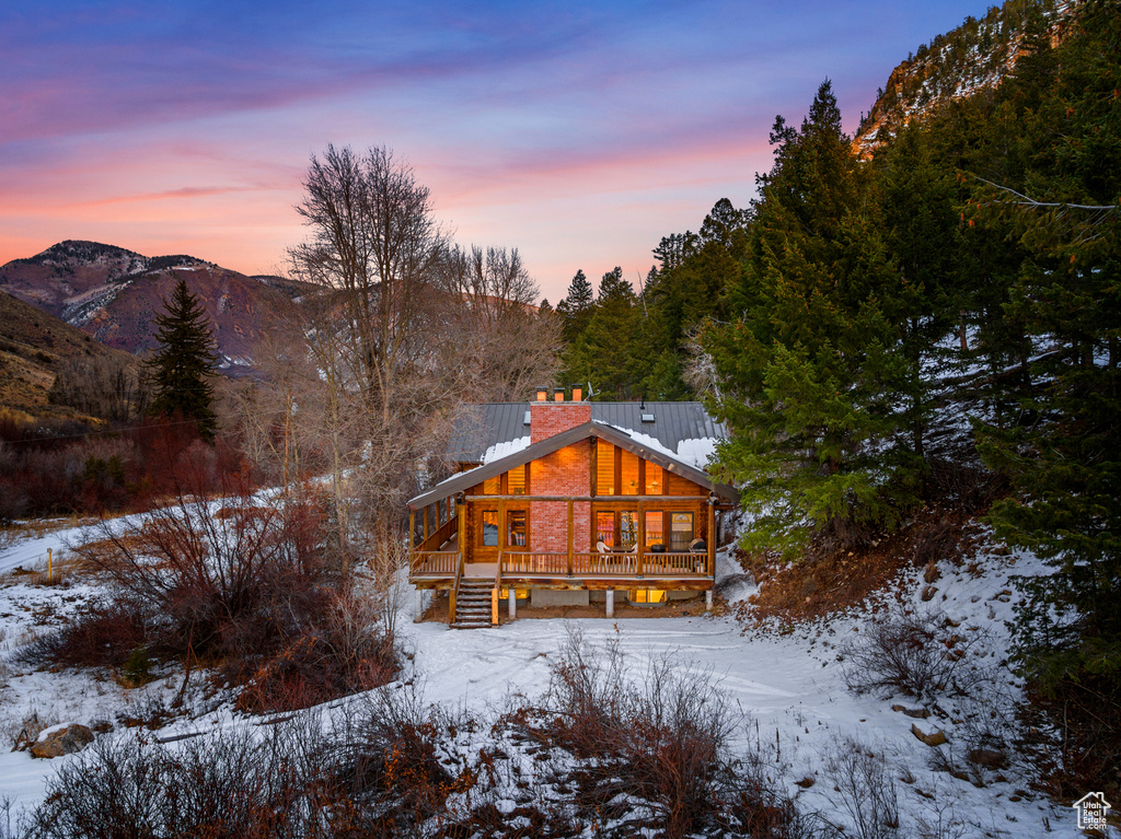 Snow covered property featuring a chimney, a wooden deck, metal roof, and a standing seam roof