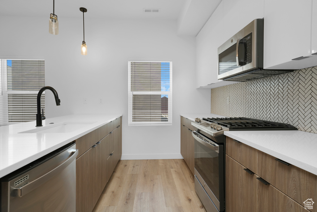 Kitchen with stainless steel appliances, a sink, backsplash, light wood finished floors, and light countertops