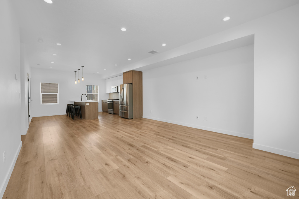 Unfurnished living room with light wood-style flooring, recessed lighting, a sink, and baseboards