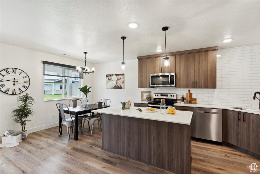 Kitchen featuring appliances with stainless steel finishes, a sink, light countertops, backsplash, and light wood finished floors