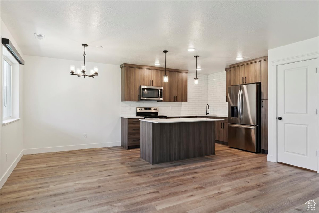 Kitchen with stainless steel appliances, a kitchen island, decorative backsplash, a chandelier, and baseboards