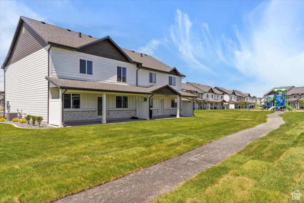 Rear view of property featuring roof with shingles, board and batten siding, a lawn, a residential view, and central air condition unit
