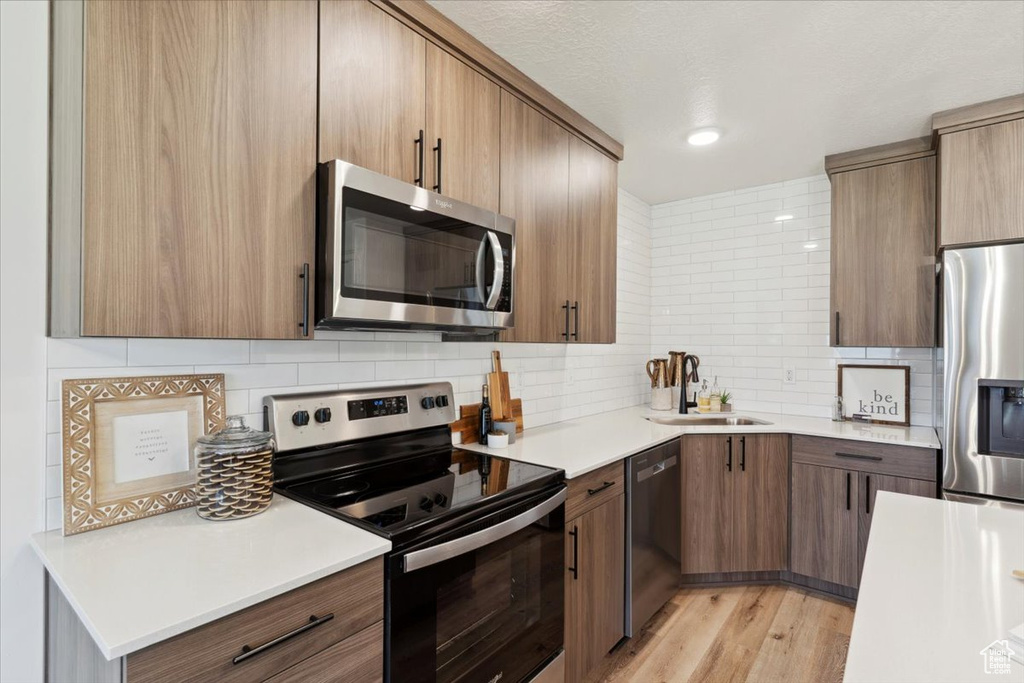Kitchen featuring appliances with stainless steel finishes, a sink, decorative backsplash, and light countertops