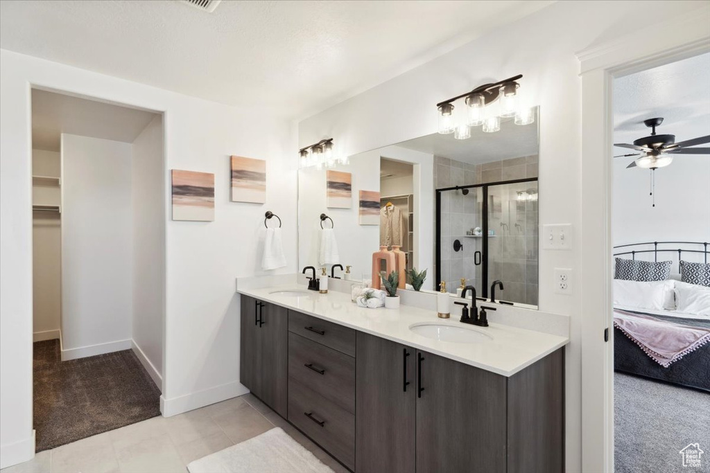 Ensuite bathroom featuring a spacious closet, double vanity, a shower stall, and a ceiling fan