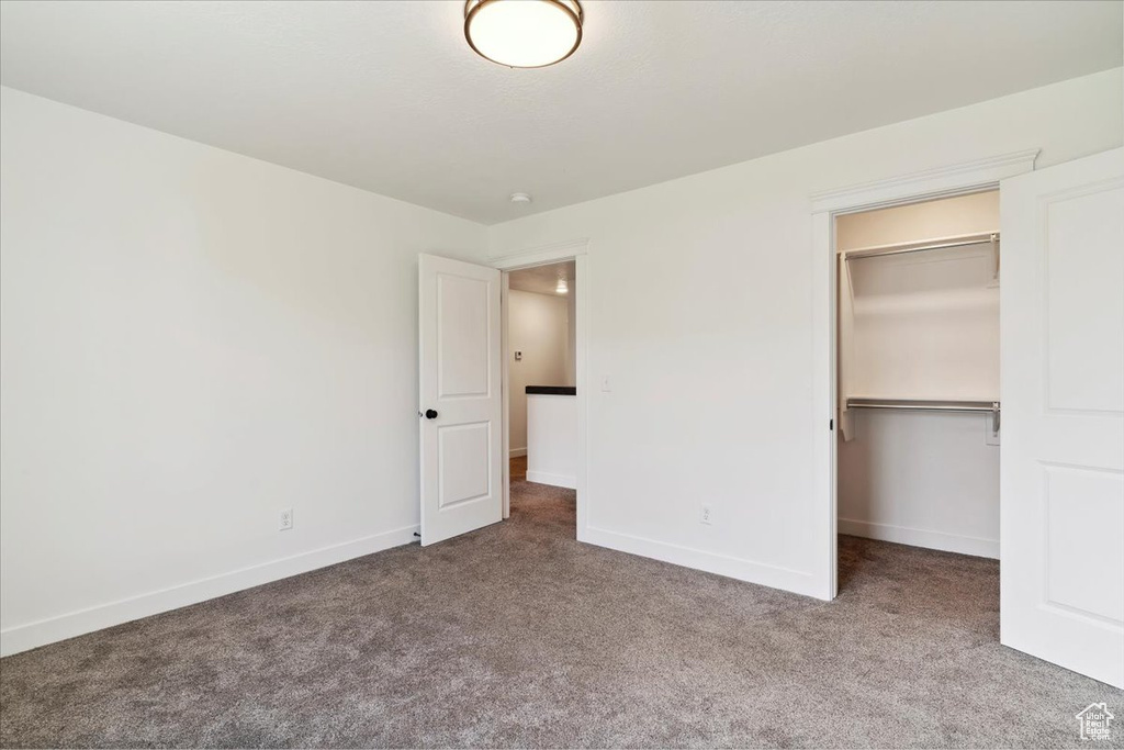 Unfurnished bedroom featuring carpet flooring, a walk in closet, baseboards, and a closet