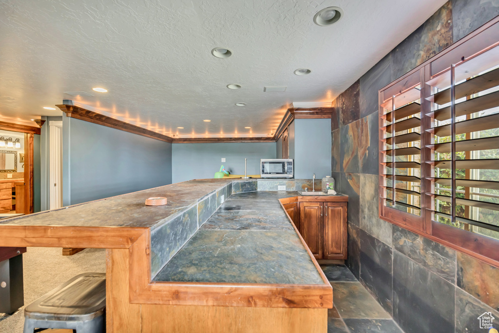Bar featuring dark stone finish floors, stainless steel microwave, recessed lighting, a sink, and crown molding