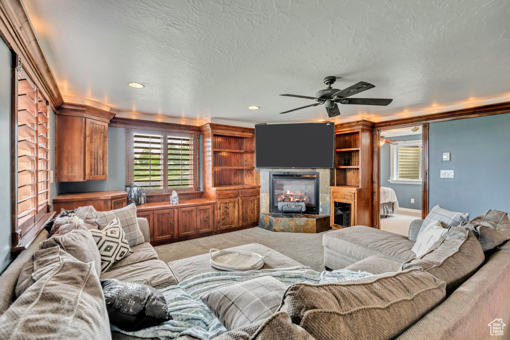 Living area featuring a tile fireplace, ceiling fan, light carpet, recessed lighting, and crown molding
