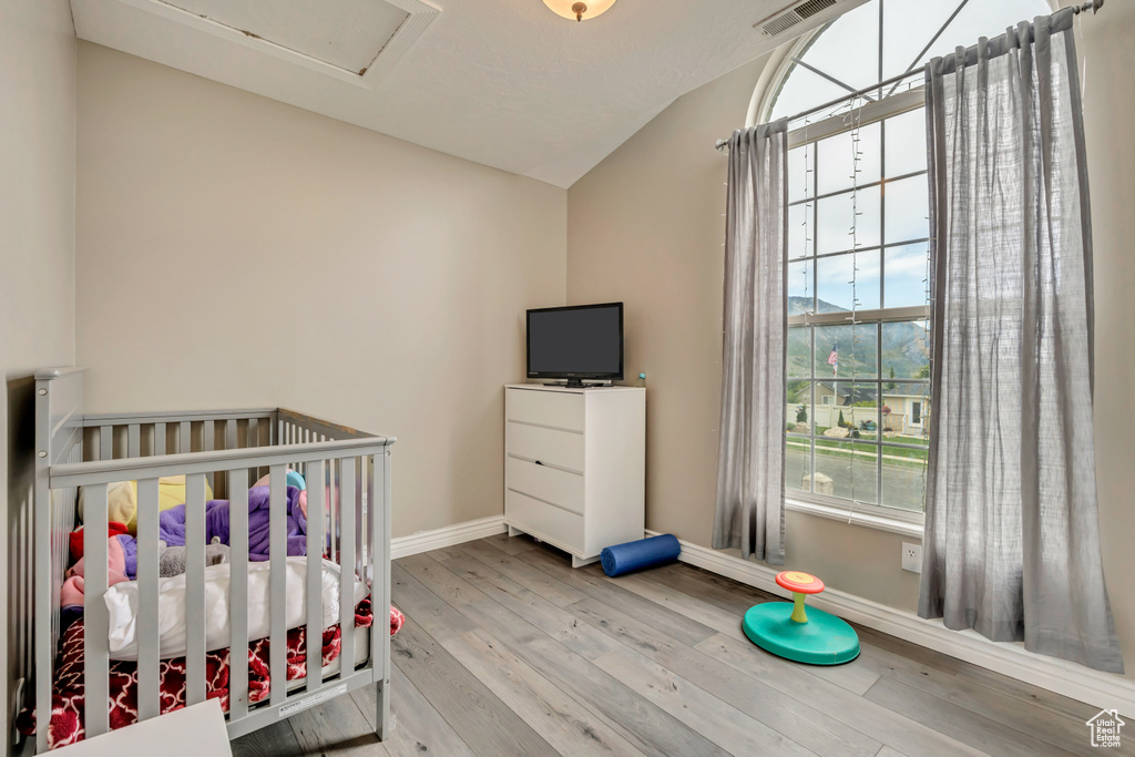 Bedroom with lofted ceiling, baseboards, wood finished floors, and a nursery area