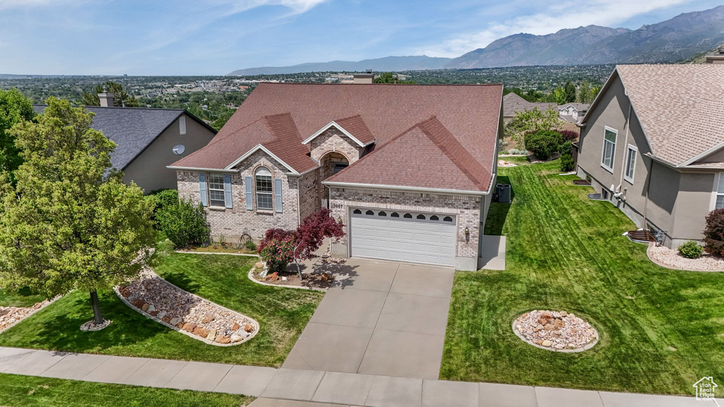 View of front of property with brick siding, driveway, an attached garage, and a front lawn
