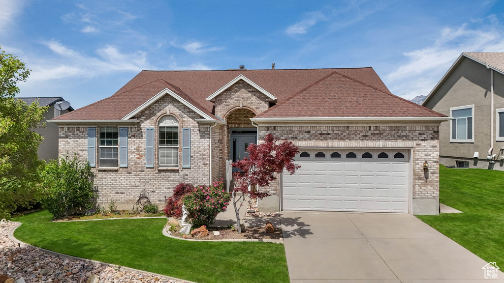 View of front facade featuring driveway, brick siding, an attached garage, a front lawn, and a shingled roof