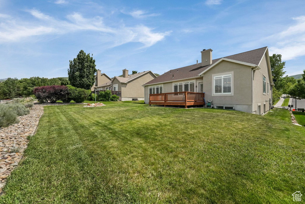 Back of property featuring a wooden deck, a lawn, and a chimney