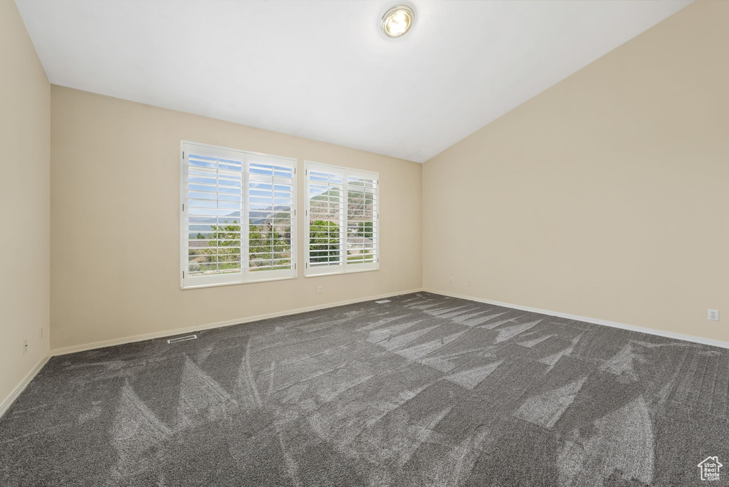 Unfurnished room featuring dark carpet, baseboards, and vaulted ceiling