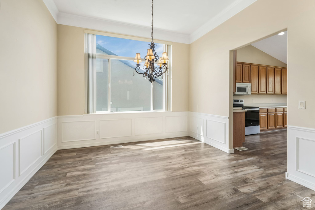 Unfurnished dining area featuring a chandelier, a decorative wall, crown molding, a wainscoted wall, and dark wood-style floors