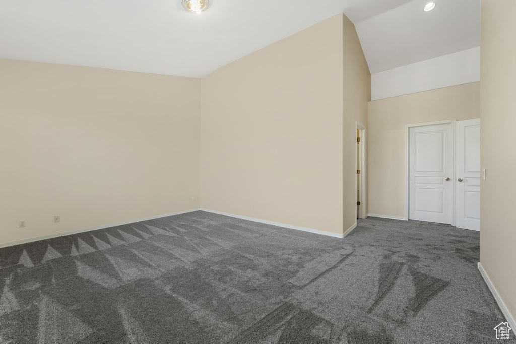 Unfurnished room with dark carpet, baseboards, and vaulted ceiling