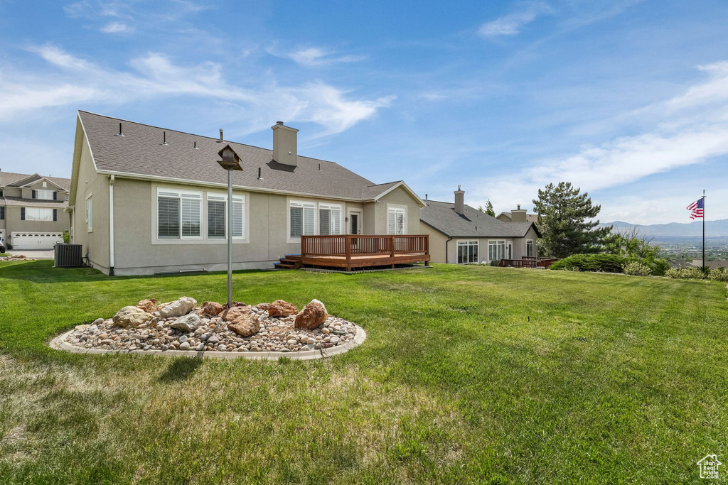 Rear view of property with central AC, a deck with mountain view, a yard, and a chimney