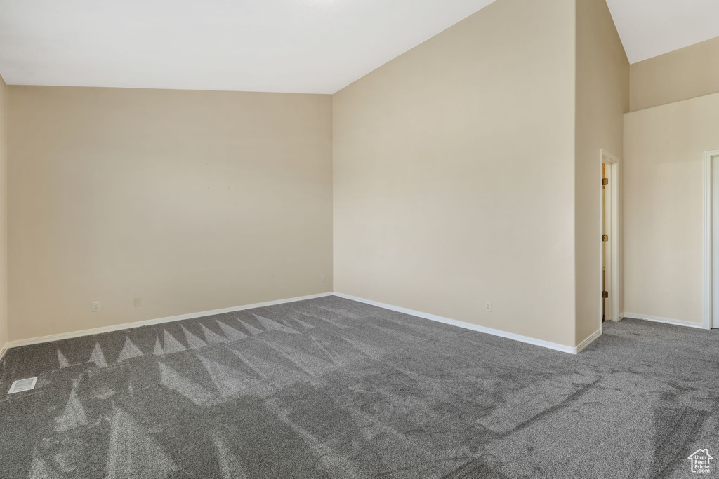 Empty room with dark colored carpet, baseboards, and lofted ceiling