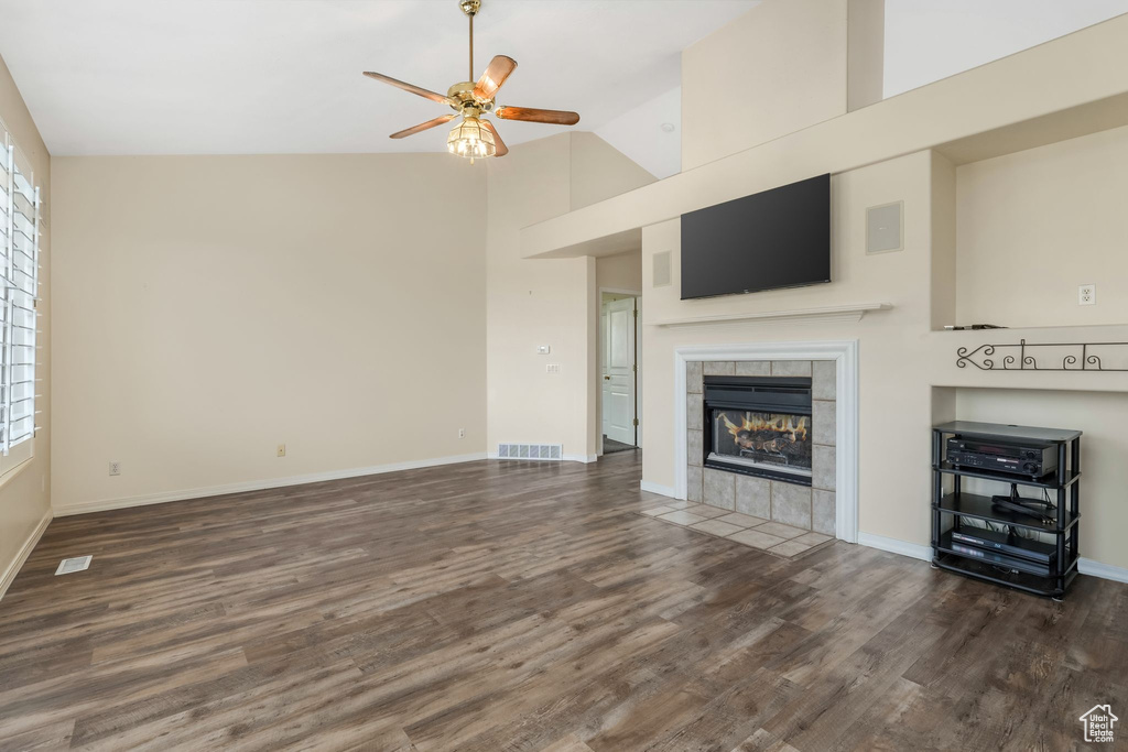 Unfurnished living room with wood finished floors, ceiling fan, a tiled fireplace, high vaulted ceiling, and baseboards