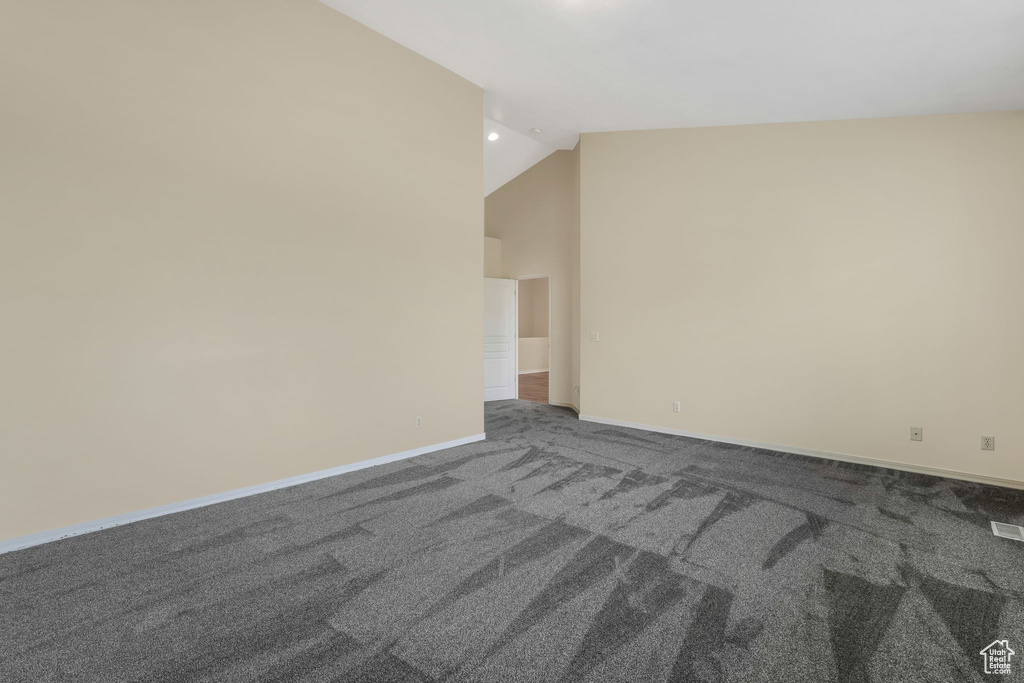 Unfurnished room with dark colored carpet, baseboards, and high vaulted ceiling