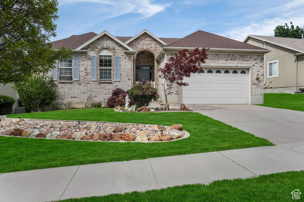 Single story home with concrete driveway, an attached garage, brick siding, a front yard, and roof with shingles