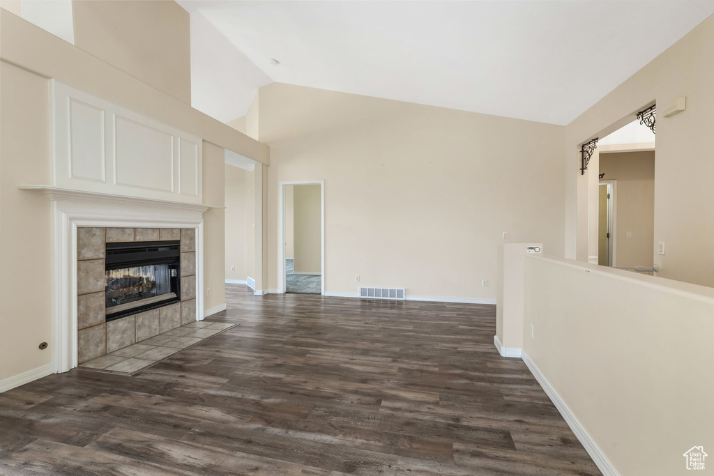 Unfurnished living room with vaulted ceiling, dark wood-type flooring, a tile fireplace, and baseboards