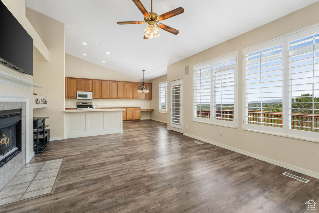 Unfurnished living room with a tile fireplace, a ceiling fan, lofted ceiling, dark wood-style flooring, and baseboards