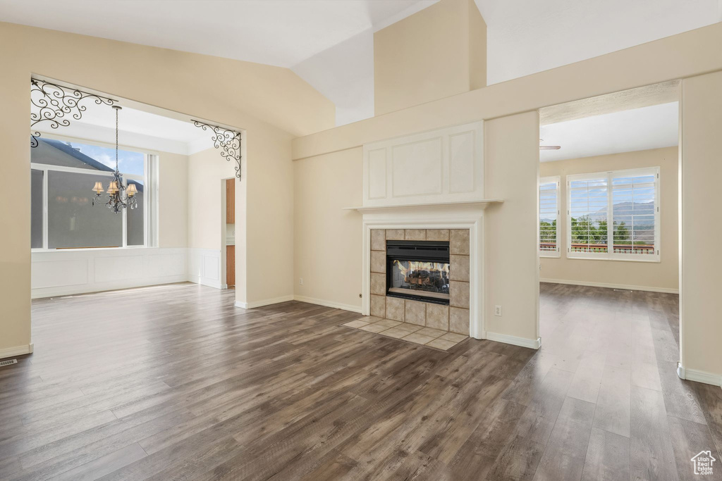 Unfurnished living room with a chandelier, dark wood finished floors, a fireplace, vaulted ceiling, and baseboards