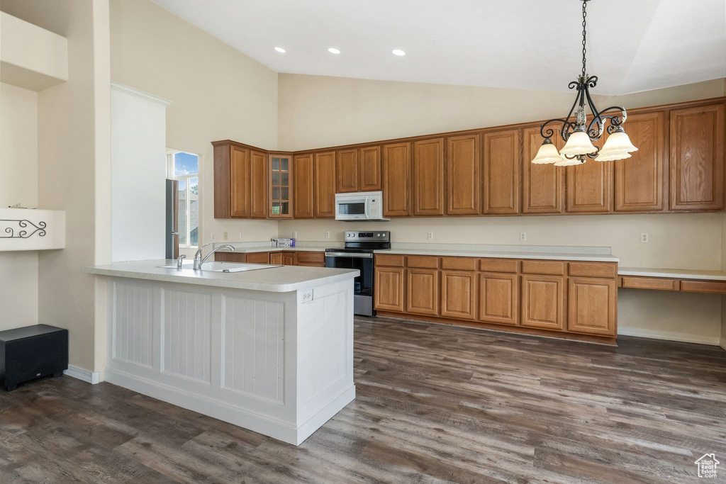 Kitchen with stainless steel electric range oven, white microwave, brown cabinetry, light countertops, and a sink