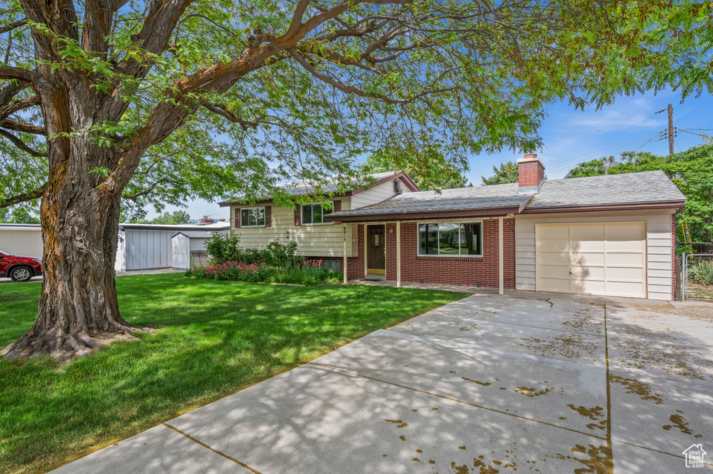 Split level home featuring a garage, driveway, brick siding, a front yard, and a chimney
