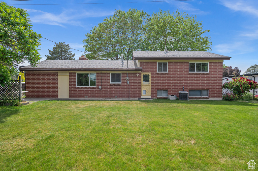Back of property featuring a lawn, brick siding, and central AC
