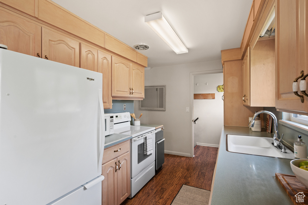 Kitchen featuring white appliances, light brown cabinetry, a sink, dark wood-style flooring, and baseboards