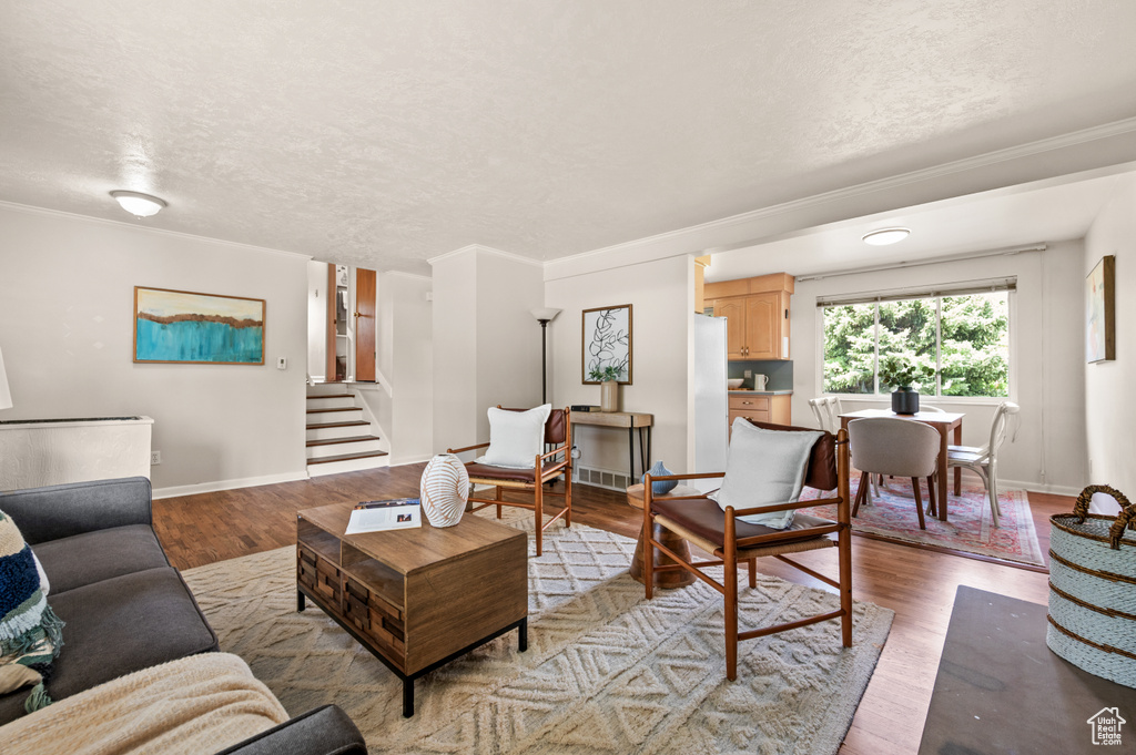 Living room featuring stairs, light wood-style flooring, a textured ceiling, ornamental molding, and baseboards