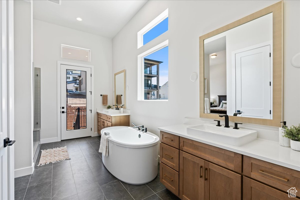 Full bathroom featuring two vanities, a freestanding tub, a stall shower, tile patterned floors, and baseboards