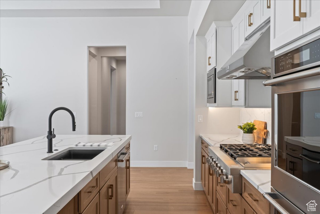 Kitchen featuring a sink, appliances with stainless steel finishes, under cabinet range hood, light wood finished floors, and baseboards