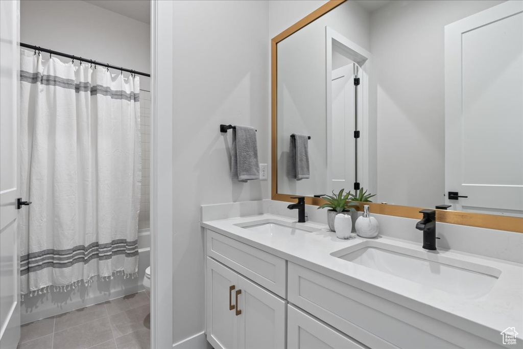 Bathroom with double vanity, toilet, shower / bath combo with shower curtain, and tile patterned flooring