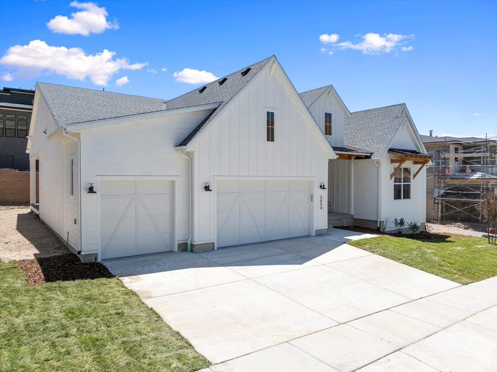Modern farmhouse with a shingled roof, concrete driveway, and board and batten siding