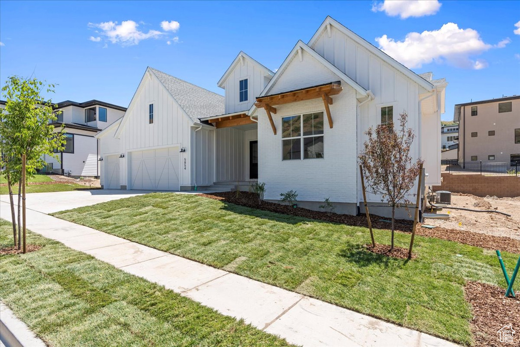Modern inspired farmhouse featuring board and batten siding, a garage, driveway, and a front yard