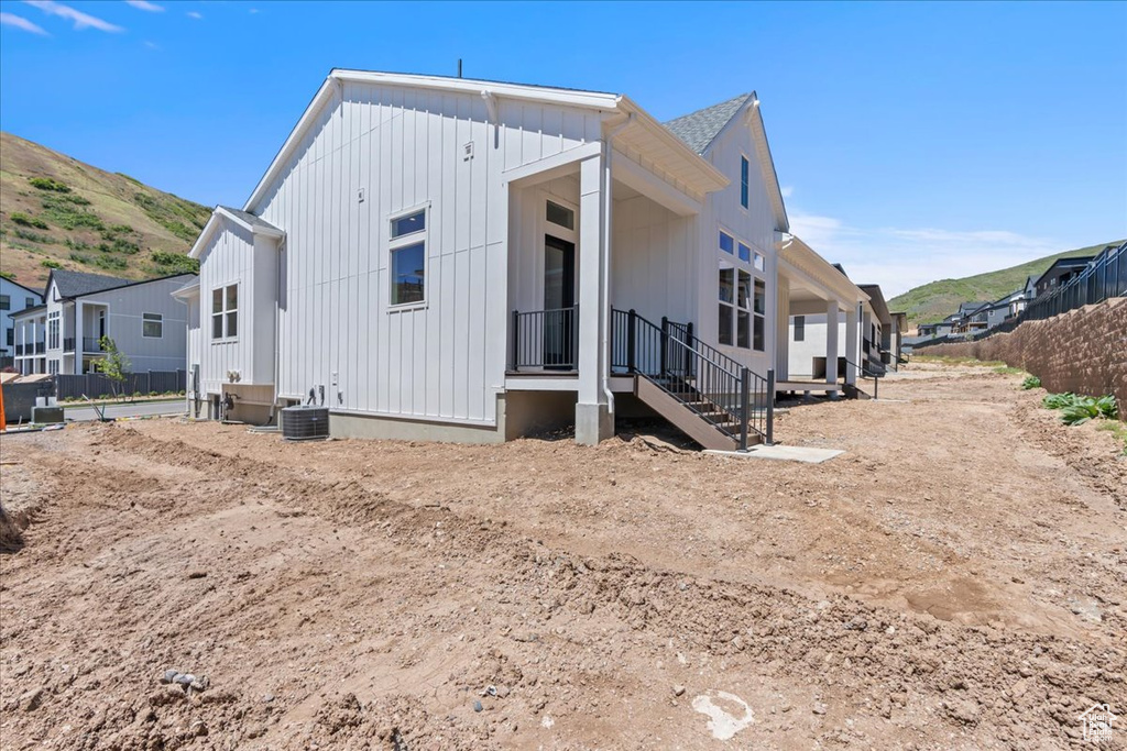 Rear view of house with board and batten siding, a mountain view, central AC unit, and a residential view