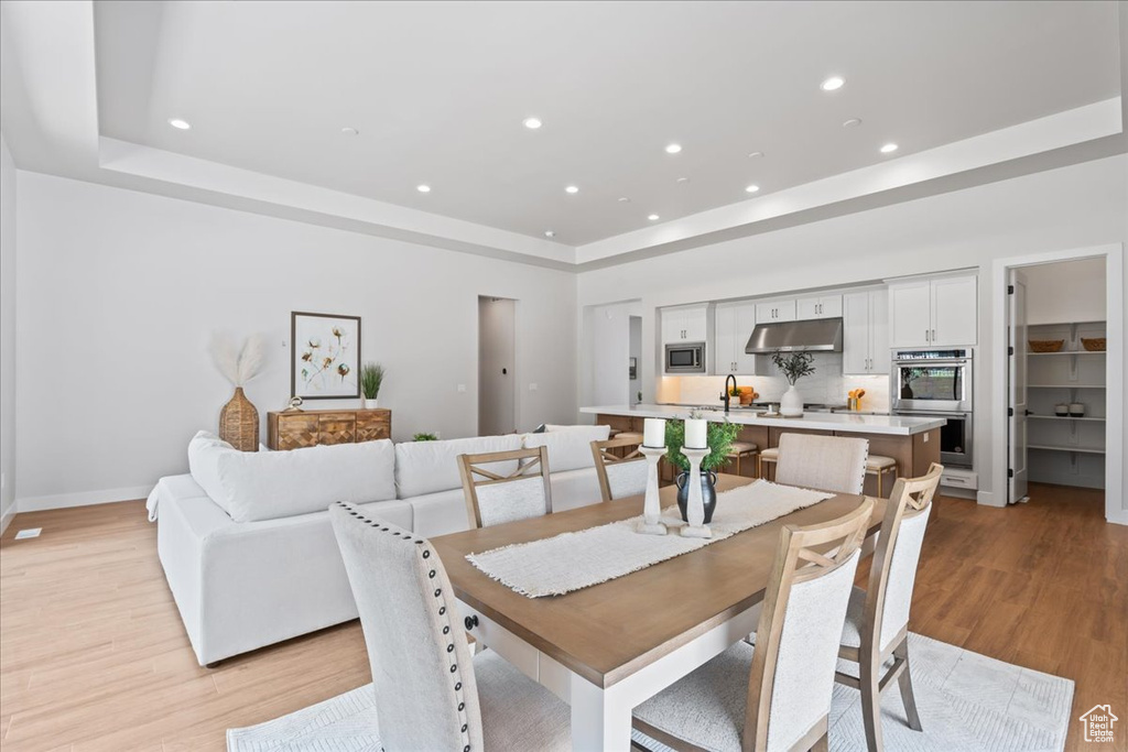 Dining area featuring a tray ceiling, light wood-style floors, recessed lighting, and baseboards