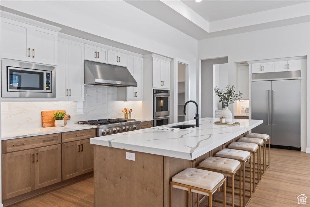Kitchen with built in appliances, under cabinet range hood, a sink, decorative backsplash, and light wood-type flooring