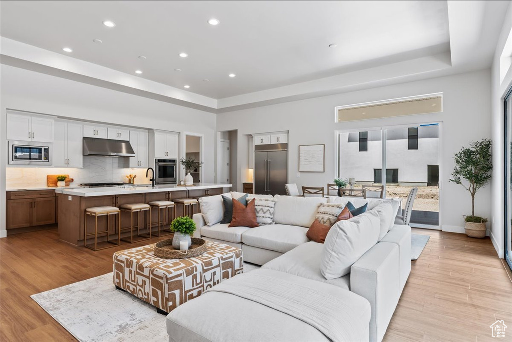 Living area featuring a raised ceiling, light wood finished floors, recessed lighting, and baseboards