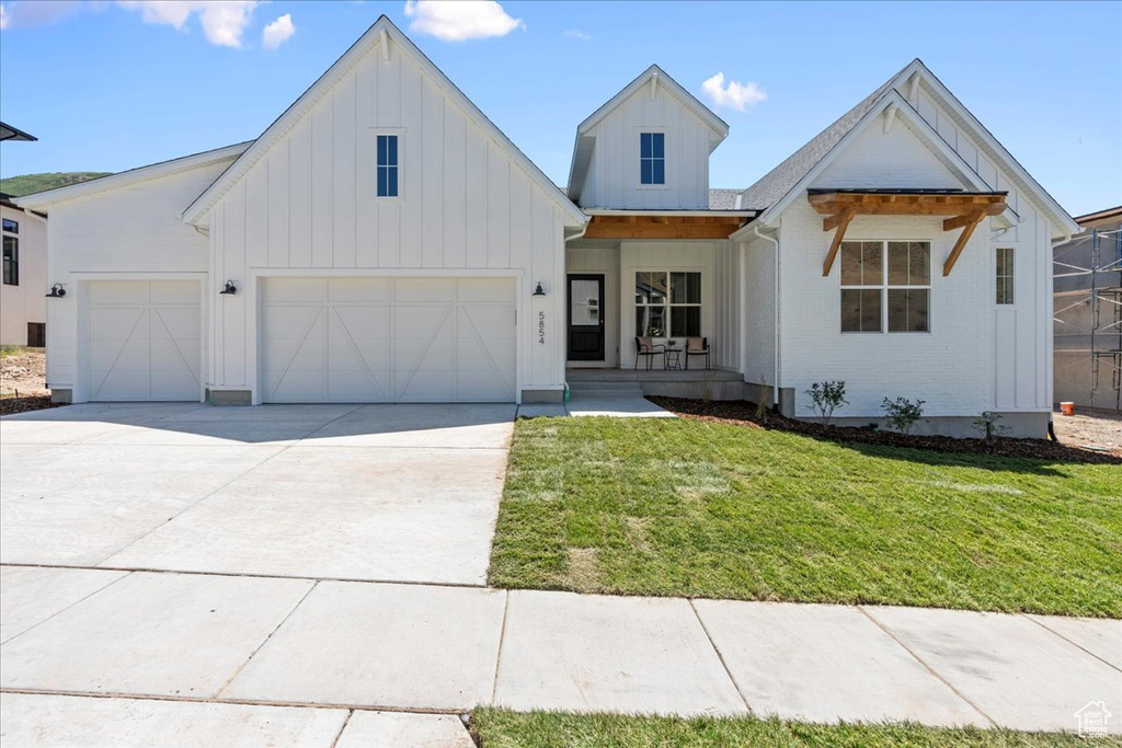 Modern farmhouse featuring board and batten siding, a front yard, a garage, concrete driveway, and a porch