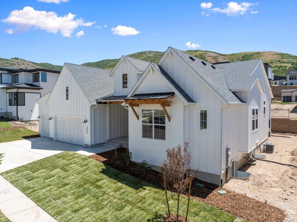 Modern inspired farmhouse featuring board and batten siding, driveway, a standing seam roof, a shingled roof, and a mountain view