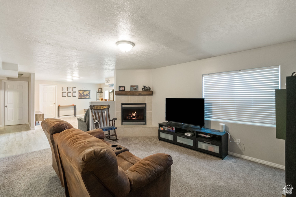 Living room with a textured ceiling, carpet floors, a tiled fireplace, and baseboards