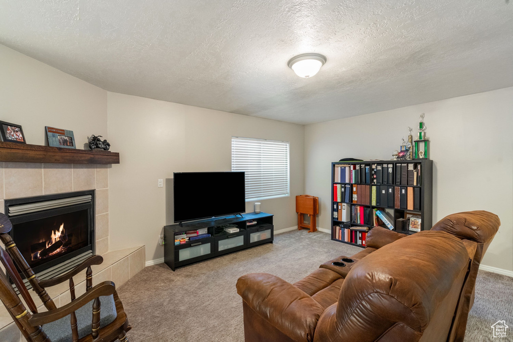 Carpeted living room with a textured ceiling, a tiled fireplace, and baseboards