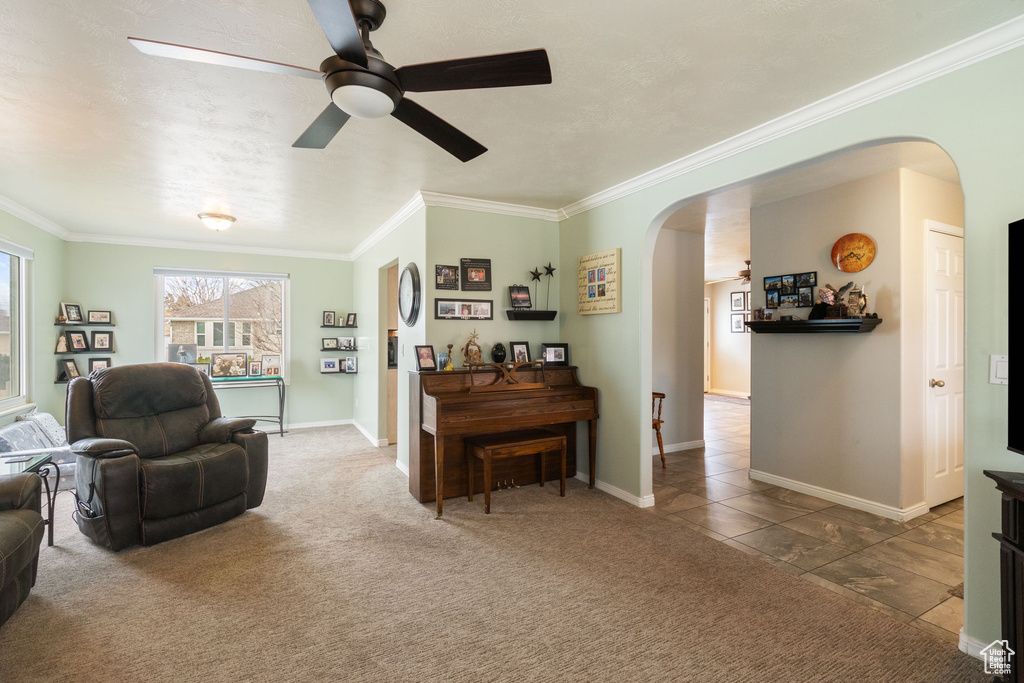 Carpeted living room with arched walkways, ceiling fan, crown molding, and baseboards