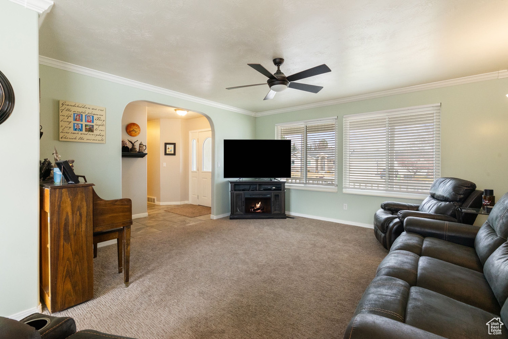 Living area featuring arched walkways, ceiling fan, ornamental molding, light carpet, and a warm lit fireplace