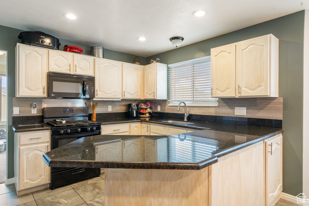 Kitchen featuring black appliances, a sink, a peninsula, decorative backsplash, and dark stone countertops