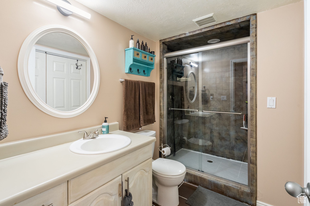 Bathroom featuring toilet, vanity, a shower stall, and a textured ceiling