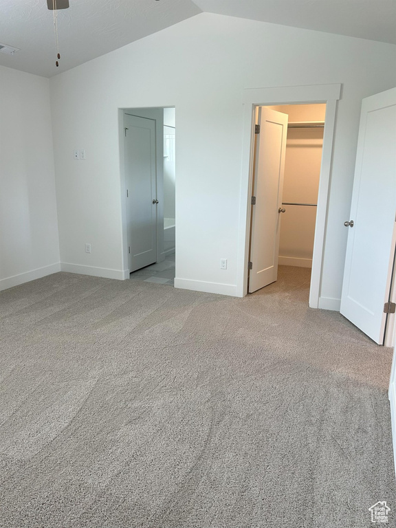 Unfurnished bedroom with lofted ceiling, a walk in closet, baseboards, carpet flooring, and a closet