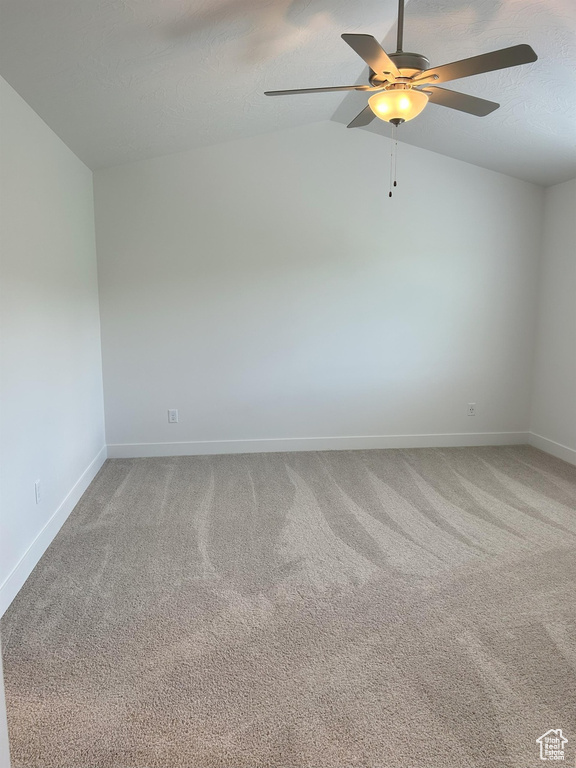 Carpeted spare room featuring a ceiling fan, baseboards, and lofted ceiling